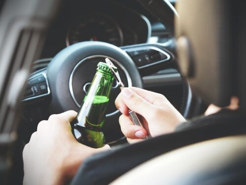 person opening a beer bottle while behind the wheel