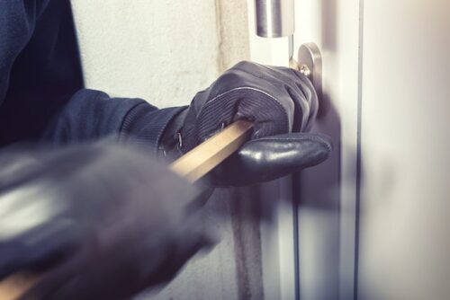 someone wearing gloves using crowbar to enter home